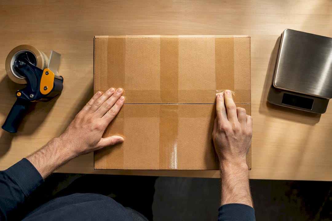 Hands applying H-taping to shipping carton